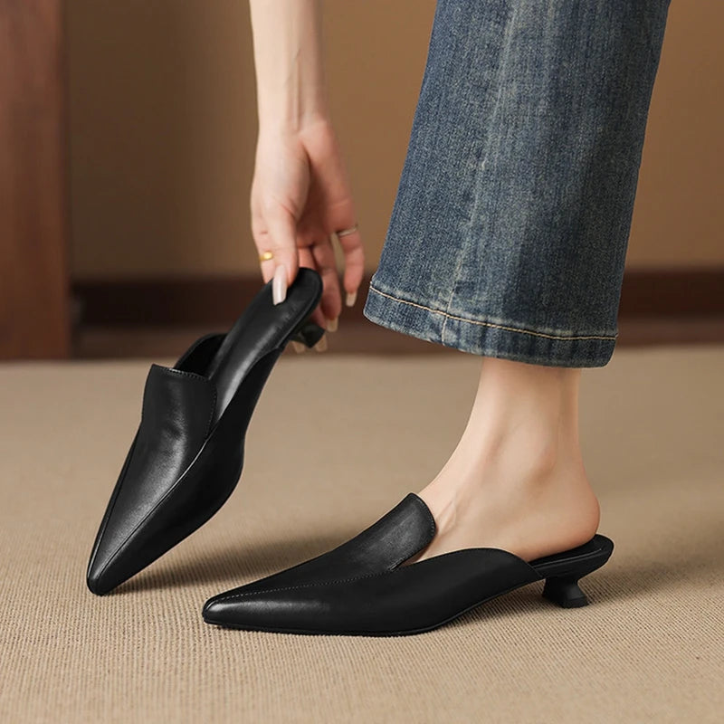 Camaiore Pointed-Toe Mules — Black, worn with blue jeans, one shoe held in hand