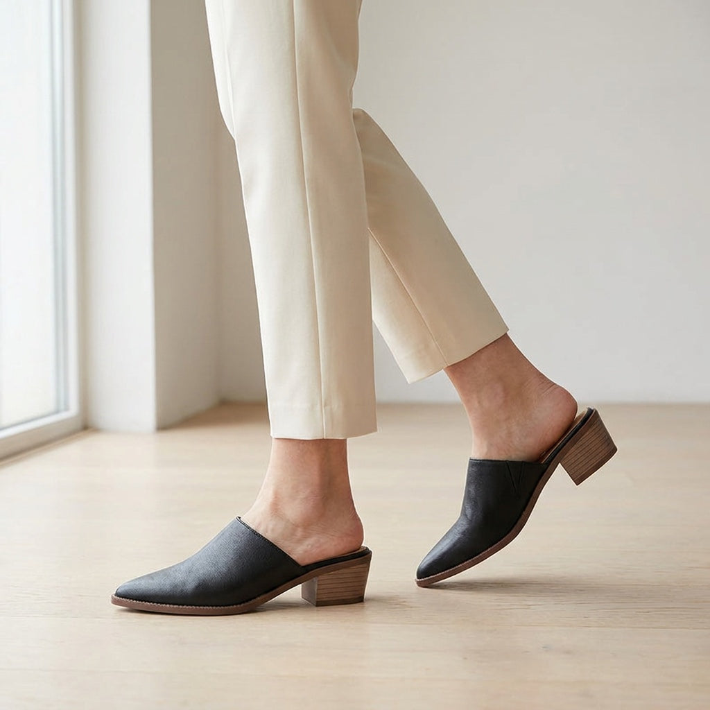 Lucera Leather Mules — Black, worn mid-stride in a gallery interior