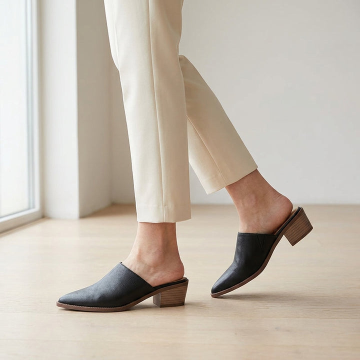 Lucera Leather Mules — Black, worn mid-stride in a gallery interior