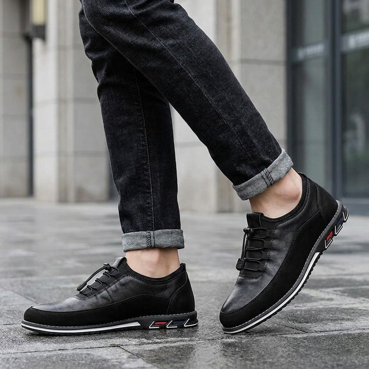 Anagni No-Tie Dress Shoes — Black, worn with dark cuffed jeans on a city sidewalk outside an office building