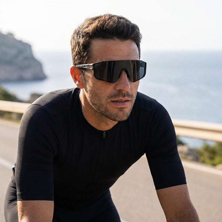 Tellaro Shield Sunglasses — Black / Smoke, worn by a man road cycling on a sunny Mallorca coast road