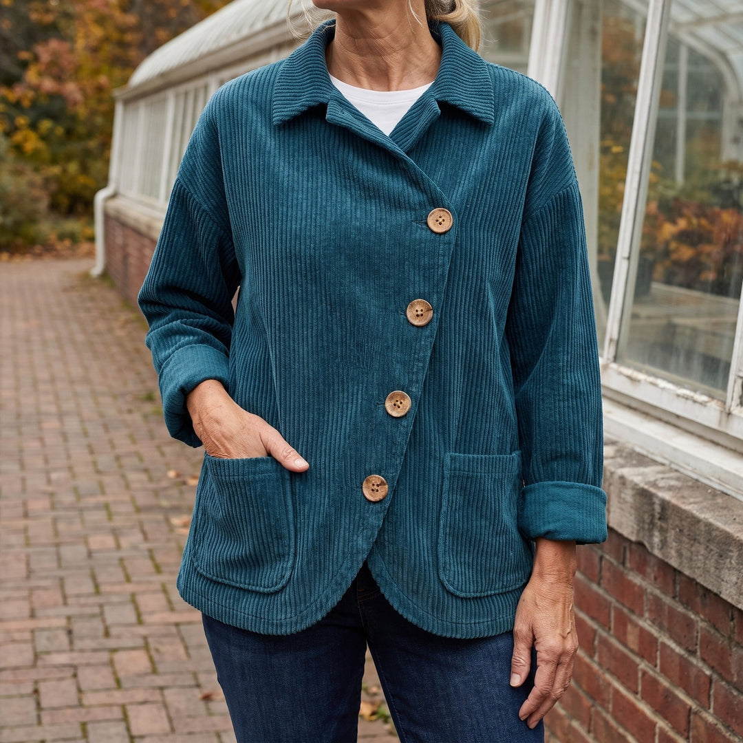 Cervinia Collared Jacket — Blue, worn by a woman with silver-blonde hair over a white tee and dark jeans, one hand in the pocket, cropped at the neck, outside a glasshouse on a brick path