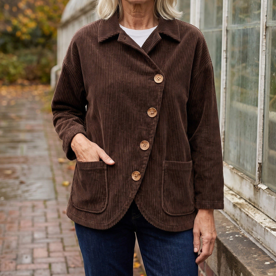 Cervinia Collared Jacket — Brown, worn by a woman with silver-blonde hair over a white tee and dark jeans, one hand in the pocket, cropped at the neck, outside a glasshouse on a brick path