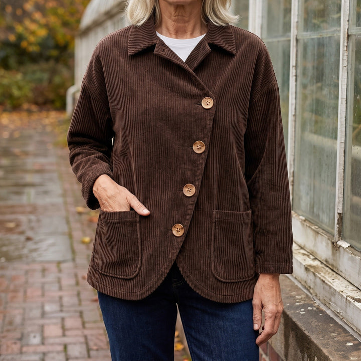 Cervinia Collared Jacket — Brown, worn by a woman with silver-blonde hair over a white tee and dark jeans, one hand in the pocket, cropped at the neck, outside a glasshouse on a brick path