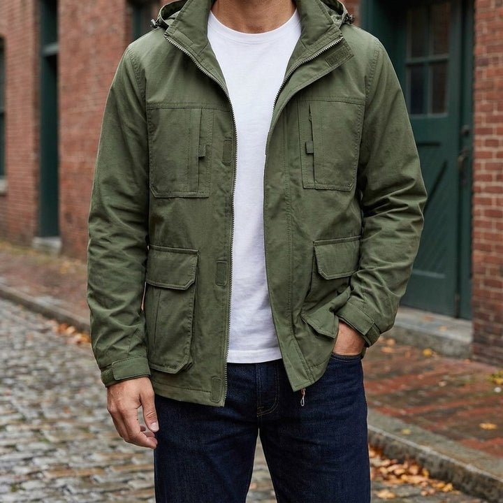 Man wearing the Faenza Hooded Cargo Jacket in Army Green open over a white tee on a brick-lined street