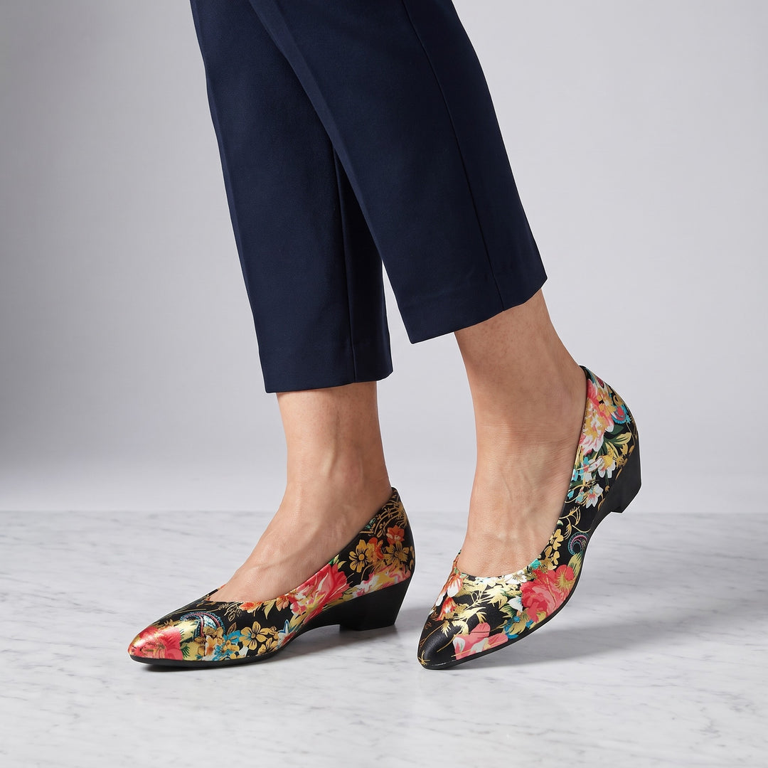 Maiori Pointed-Toe Pumps — Black Floral, worn by a woman in navy cropped trousers, knee down, on marble