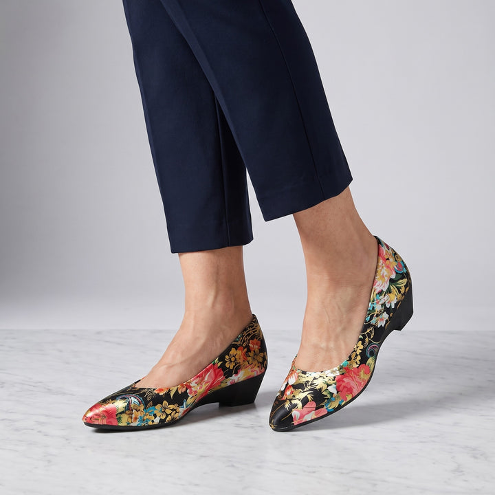 Maiori Pointed-Toe Pumps — Black Floral, worn by a woman in navy cropped trousers, knee down, on marble