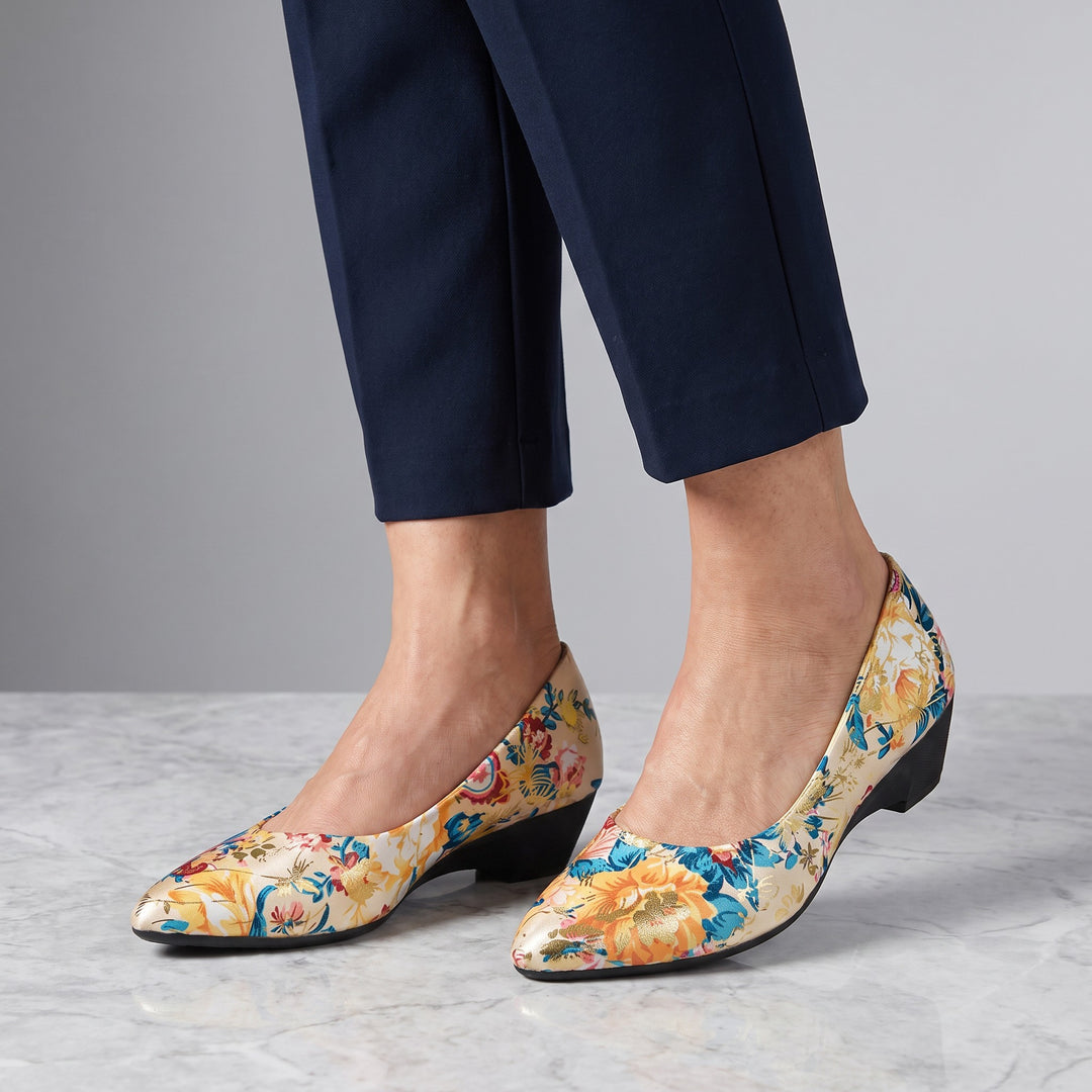 Maiori Pointed-Toe Pumps — Cream Floral, worn by a woman in navy cropped trousers, knee down, on marble