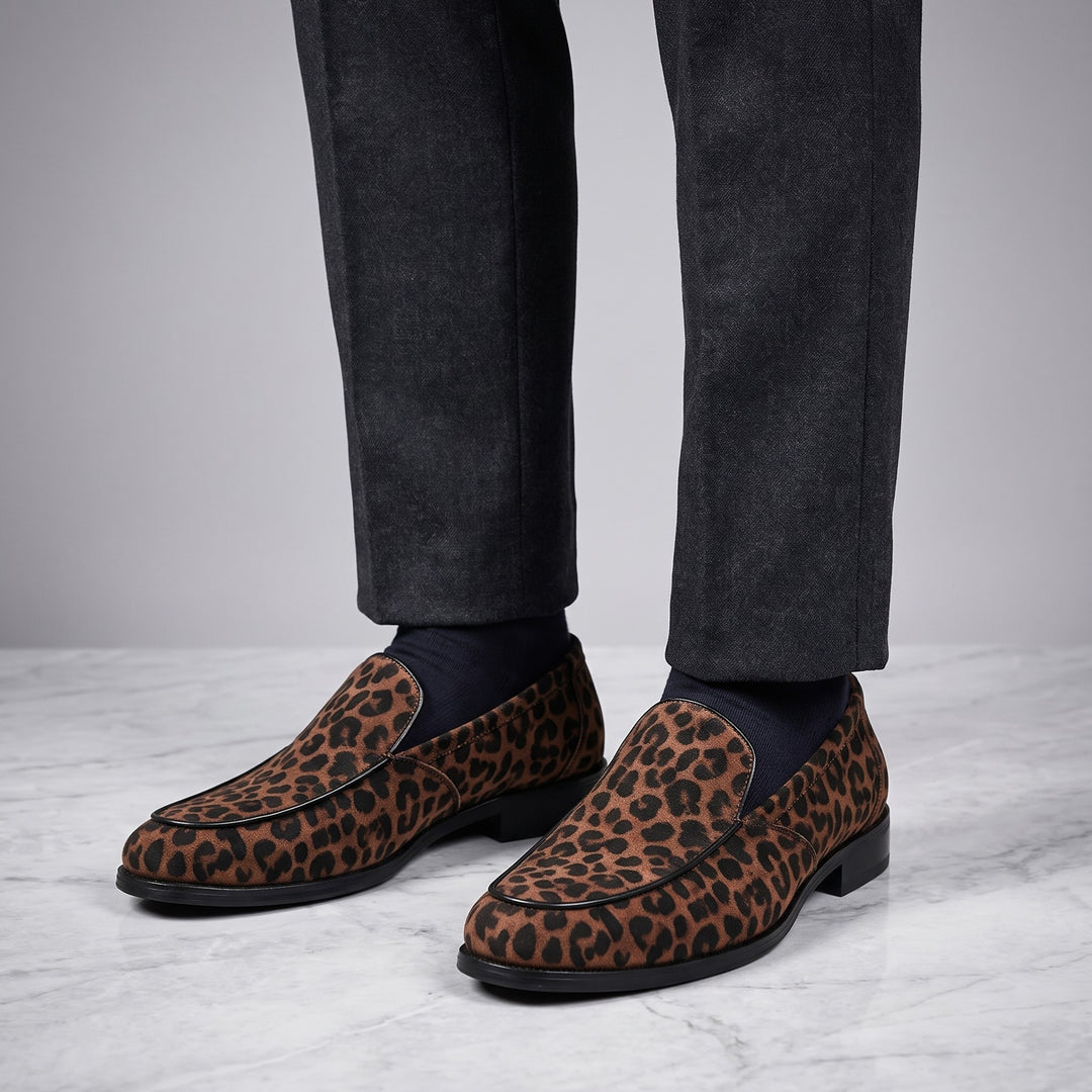 Mantova Suede Loafers — Brown Leopard, worn by a man in charcoal trousers, knee down, on marble
