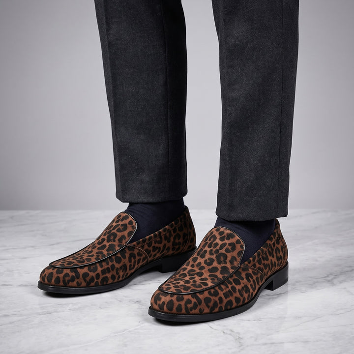 Mantova Suede Loafers — Brown Leopard, worn by a man in charcoal trousers, knee down, on marble